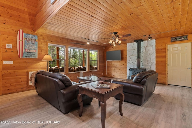 living area featuring wooden walls, a wood stove, light wood-type flooring, wood ceiling, and a ceiling fan