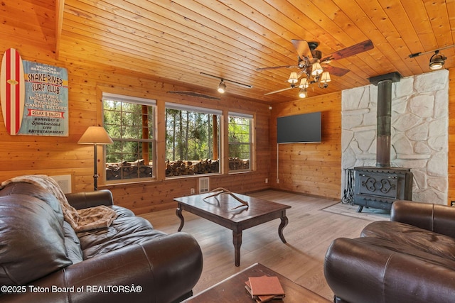 living room featuring wood walls, track lighting, wooden ceiling, wood finished floors, and a wood stove