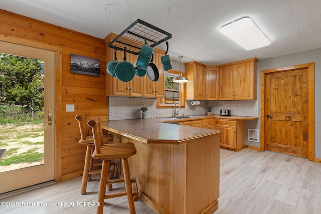 kitchen featuring a sink, a peninsula, light wood-style floors, tasteful backsplash, and a breakfast bar area