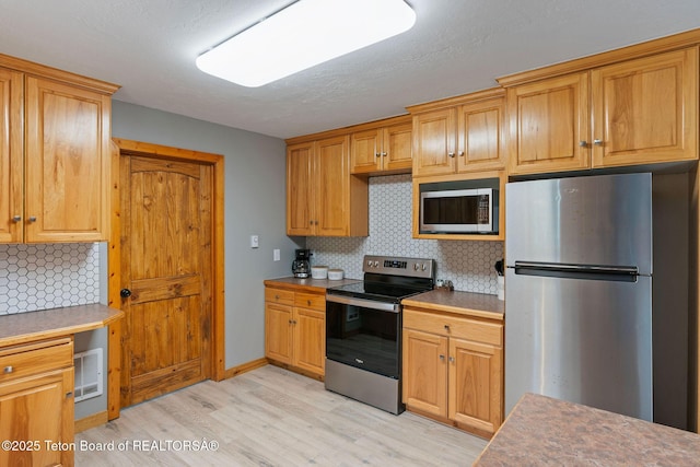 kitchen with stainless steel appliances, light wood finished floors, and tasteful backsplash