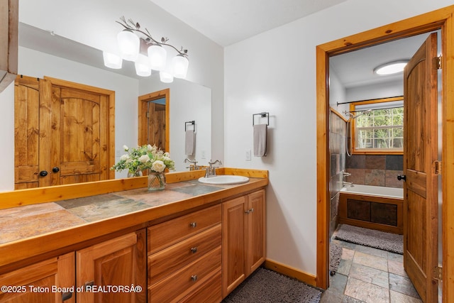 full bathroom featuring baseboards, stone tile flooring, a tub, vanity, and a shower