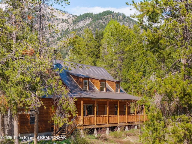 back of property featuring a porch, a mountain view, metal roof, and a forest view