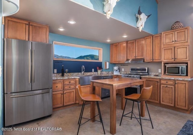 kitchen featuring appliances with stainless steel finishes, a sink, recessed lighting, brown cabinets, and under cabinet range hood