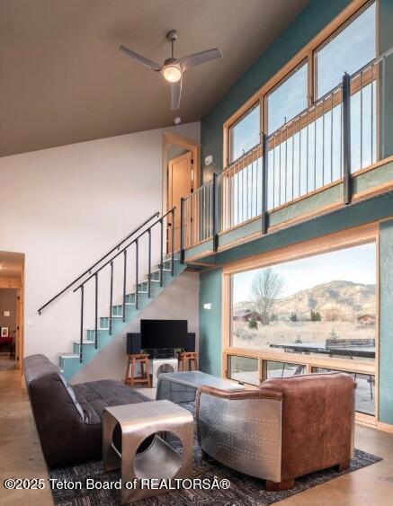 living area with a high ceiling, stairway, and ceiling fan