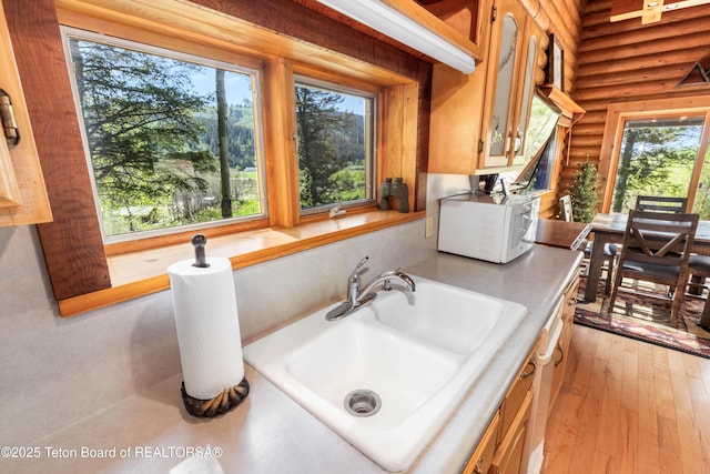 185 River Bench Rd, Thayne, WY 83127 - kitchen view of a sink, rustic walls, white microwave, light countertops, and glass insert cabinets