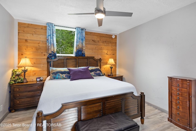 366 E 5th Ave, Afton, WY 83110 - bedroom with light wood-style flooring, wooden walls, baseboards, a textured ceiling, and ceiling fan