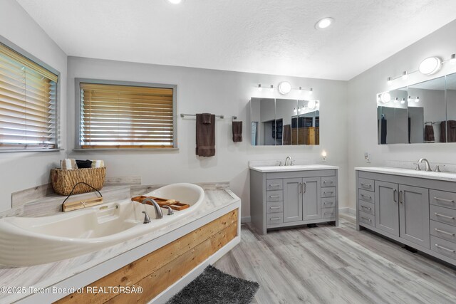 366 E 5th Ave, Afton, WY 83110 - bathroom with two vanities, a bath, wood finished floors, recessed lighting, and a textured ceiling