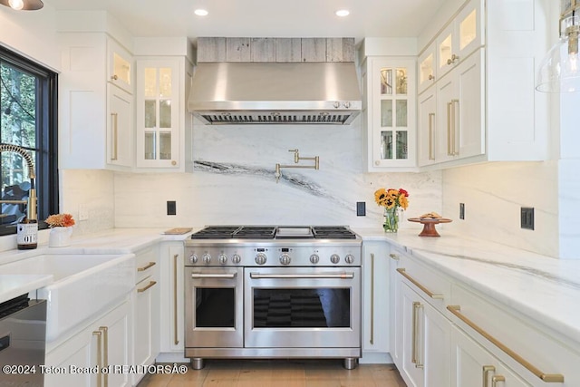 kitchen featuring double oven range, wall chimney exhaust hood, dishwasher, white cabinetry, and recessed lighting