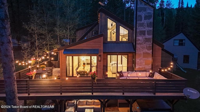 back of house at night with a wooden deck, metal roof, and a standing seam roof