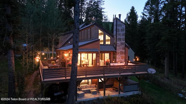 back of house with a patio area, a deck, outdoor lounge area, metal roof, and a chimney