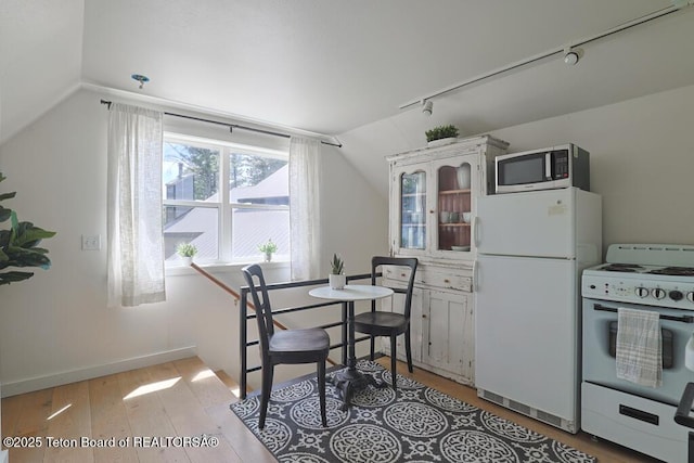 dining room with rail lighting, lofted ceiling, light wood finished floors, and baseboards