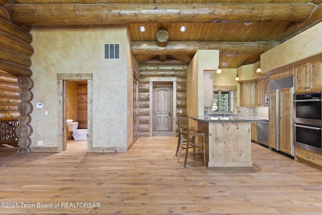 5725 W Caddis Fly Dr, Wilson, WY 83014 - kitchen featuring log walls, a wooden ceiling with exposed beams, appliances with stainless steel finishes, a towering ceiling, and light wood-style floors