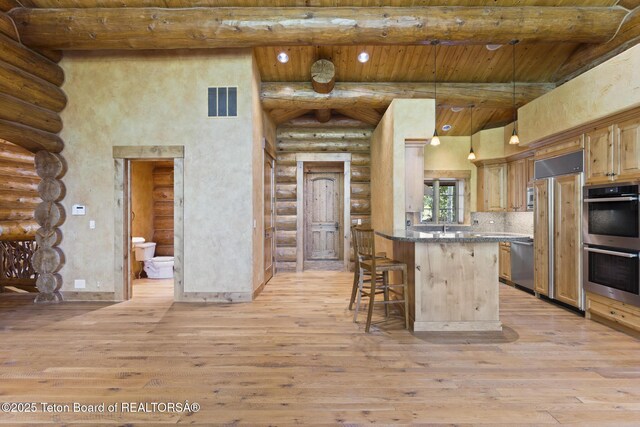 5725 W Caddis Fly Dr, Wilson, WY 83014 - kitchen featuring log walls, a wooden ceiling with exposed beams, appliances with stainless steel finishes, a towering ceiling, and light wood-style floors
