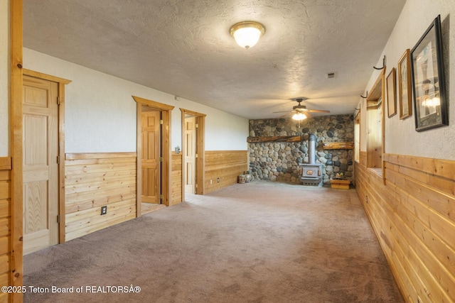 188 E 3000 S, Driggs, ID 83422 - unfurnished living room with a wood stove, wainscoting, wooden walls, a textured ceiling, and ceiling fan