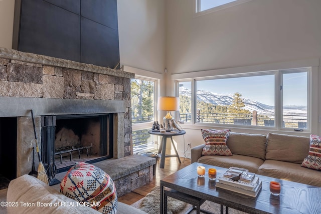 6960 Lupine Trl, Wilson, WY 83001 - living area featuring healthy amount of natural light, wood finished floors, a stone fireplace, a mountain view, and a high ceiling
