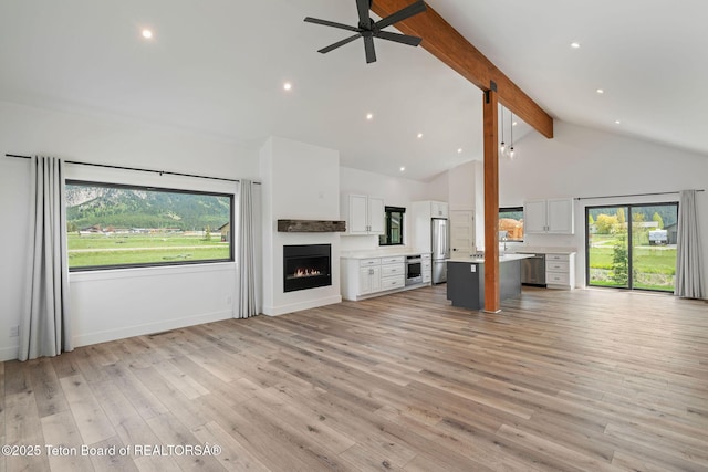 185 Columbine St, Alpine, WY 83128 - unfurnished living room featuring beamed ceiling, healthy amount of natural light, a warm lit fireplace, a ceiling fan, and high vaulted ceiling