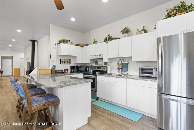 279 Vista E Dr, Star Valley Ranch, WY 83127 - kitchen with stainless steel appliances, under cabinet range hood, a breakfast bar area, light wood finished floors, and white cabinetry