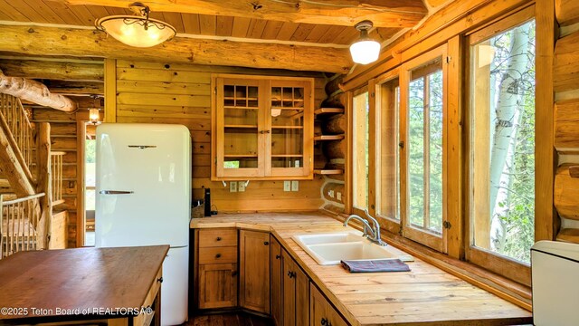 10559 Rammell Mountain Rd, Tetonia, ID 83452 - kitchen with freestanding refrigerator, log walls, wooden ceiling with exposed beams, a sink, and wooden counters
