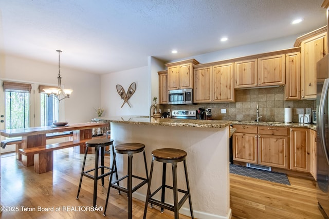 125 Cobble Creek Ln Unit 75, Driggs, ID 83422 - kitchen with stainless steel microwave, stove, light wood finished floors, decorative backsplash, and a kitchen breakfast bar