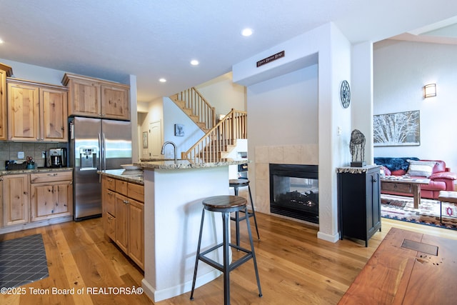 125 Cobble Creek Ln Unit 75, Driggs, ID 83422 - kitchen featuring stainless steel refrigerator with ice dispenser, a kitchen breakfast bar, light wood-style flooring, light stone counters, and backsplash
