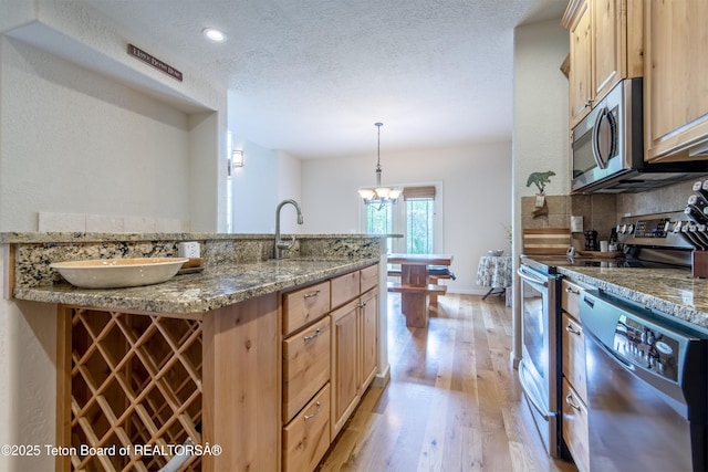 125 Cobble Creek Ln Unit 75, Driggs, ID 83422 - kitchen featuring appliances with stainless steel finishes, a sink, light wood-style floors, decorative backsplash, and a textured ceiling