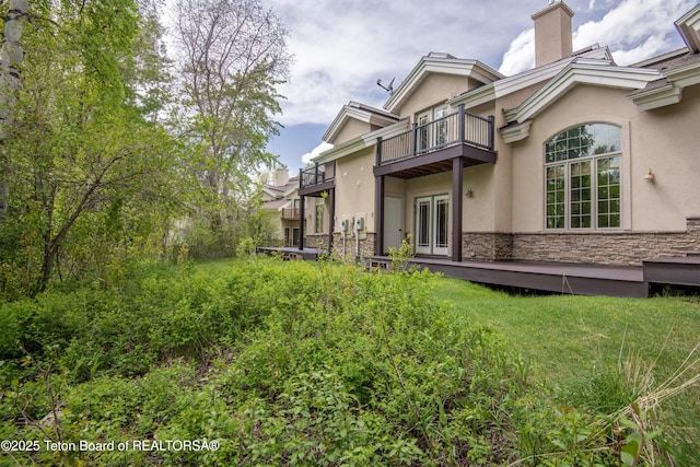 125 Cobble Creek Ln Unit 75, Driggs, ID 83422 - back of house with a balcony, stone siding, a chimney, and stucco siding