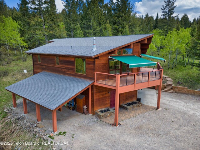 3190 Sorensen Creek Dr, Victor, ID 83455 - back of property featuring a shingled roof, a wooden deck, a forest view, and driveway