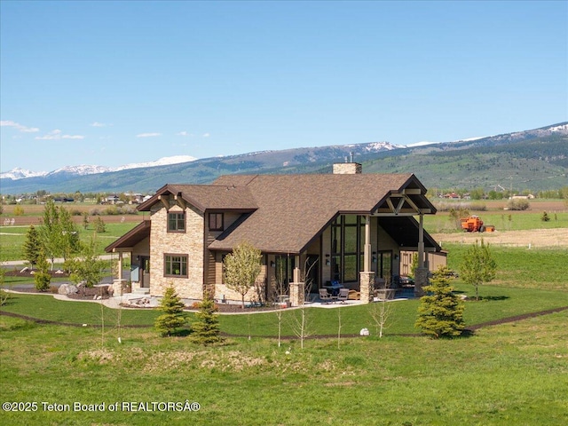 1795 Fumarole Dr, Victor, ID 83455 - view of front of house featuring stone siding, a mountain view, a patio area, a front lawn, and a chimney