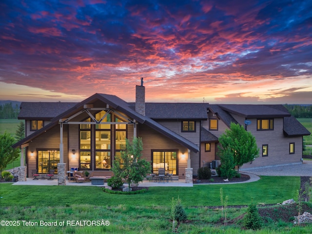 1795 Fumarole Dr, Victor, ID 83455 - back of house at dusk with a chimney, a patio area, a lawn, and a shingled roof