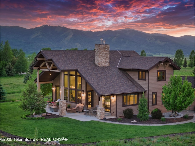 1795 Fumarole Dr, Victor, ID 83455 - back of property at dusk featuring a chimney, roof with shingles, a mountain view, and a lawn