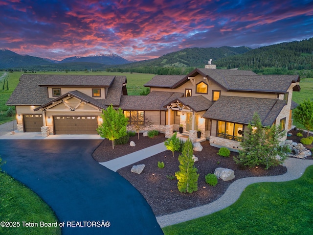 1795 Fumarole Dr, Victor, ID 83455 - view of front of home with stone siding, a mountain view, driveway, and a garage