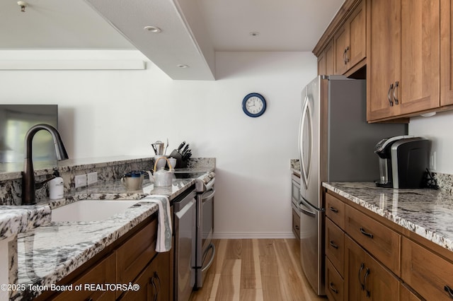 3946 Lake Creek Dr Unit 1-1-1, Wilson, WY 83014 - kitchen featuring brown cabinets, a sink, light stone countertops, appliances with stainless steel finishes, and light wood-style floors
