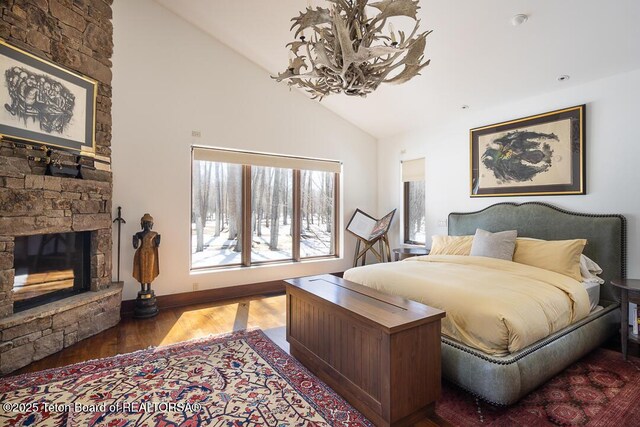 1120 S Thunder Rd, Wilson, WY 83014 - bedroom featuring a chandelier, wood finished floors, a fireplace, high vaulted ceiling, and baseboards