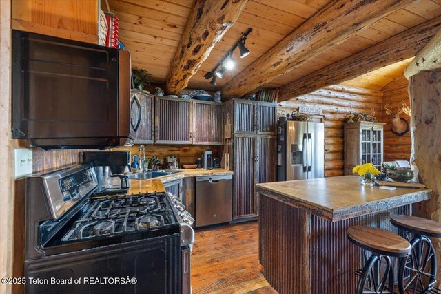 62 Skyline Dr, Bondurant, WY 82922 - kitchen with appliances with stainless steel finishes, rustic walls, a sink, wood finished floors, and wooden ceiling with exposed beams