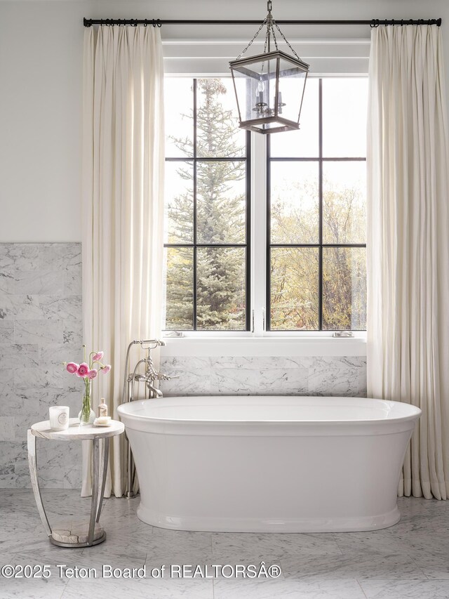 5025 Shoshone Dr, Wilson, WY 83014 - full bath featuring tile walls, a chandelier, a freestanding bath, and marble look tiles