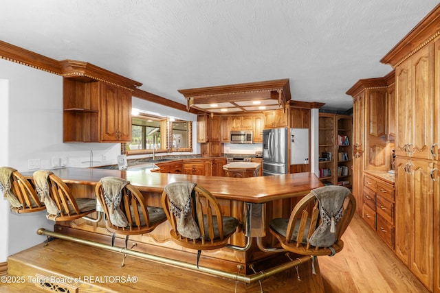 1255 Lost Crk, Thayne, WY 83127 - kitchen featuring appliances with stainless steel finishes, open shelves, light wood-style flooring, a sink, and a peninsula