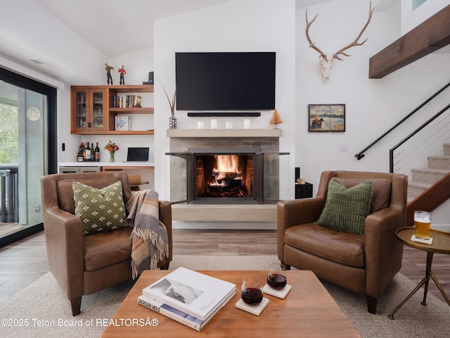7280 N Rachel Way Unit B-7, Teton Village, WY 83025 - living room featuring a warm lit fireplace, light wood-style flooring, vaulted ceiling, and stairway