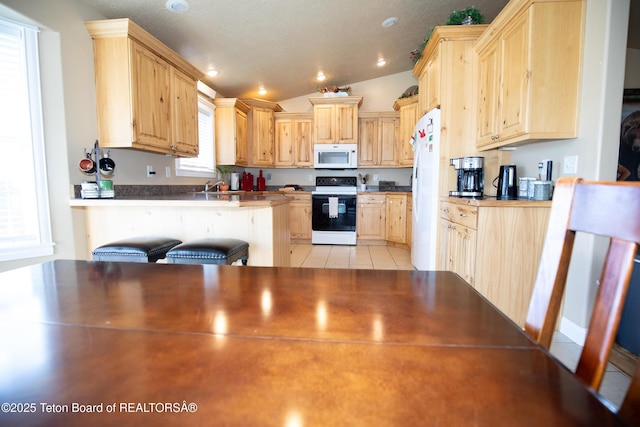28 Brushwood Dr, Star Valley Ranch, WY 83127 - kitchen featuring white appliances, light brown cabinetry, a peninsula, vaulted ceiling, and light tile patterned floors
