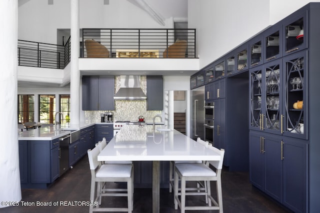 185 S Swan Rd, Jackson, WY 83001 - kitchen with wall chimney exhaust hood, blue cabinets, a high ceiling, a breakfast bar, and glass insert cabinets