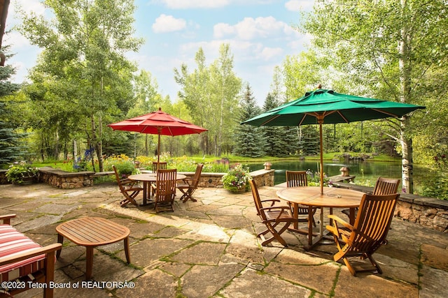 view of patio with outdoor dining area, view of wooded area, and a water view