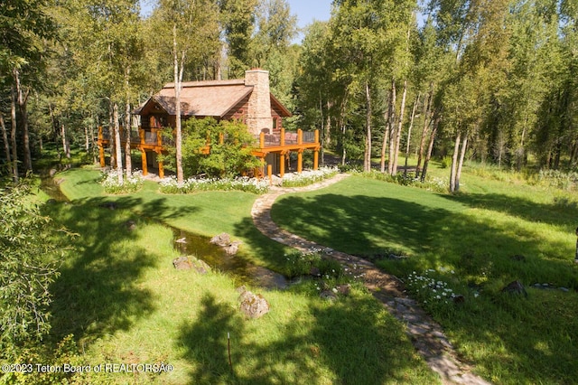 view of green lawn with a wooden deck and a view of trees