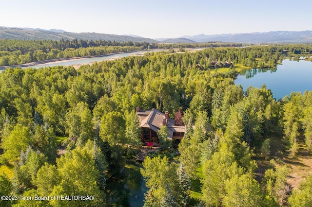 aerial view of property and surrounding area featuring a forest and a water and mountain view