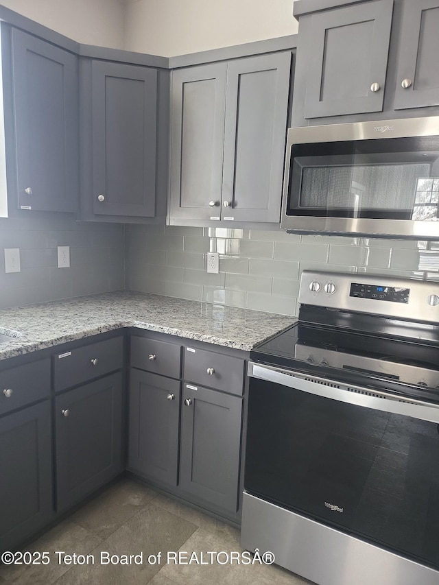 360 Wooden Spur Dr, Alpine, WY 83128 - kitchen with stainless steel appliances, gray cabinetry, decorative backsplash, and light stone counters