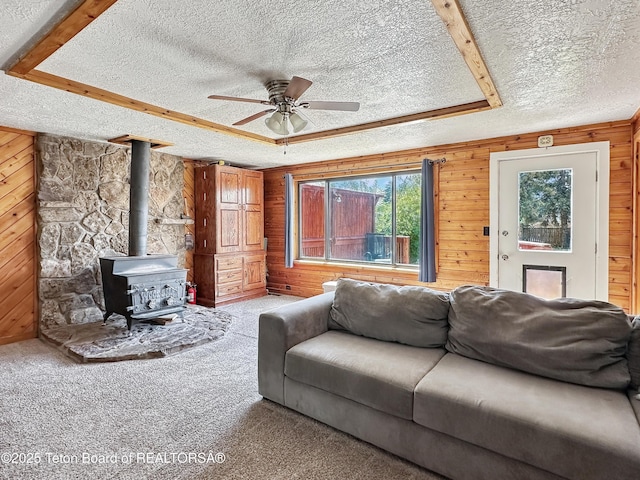 566 Jefferson St, Afton, WY 83110 - living area featuring a textured ceiling, wooden walls, a wood stove, ceiling fan, and carpet floors