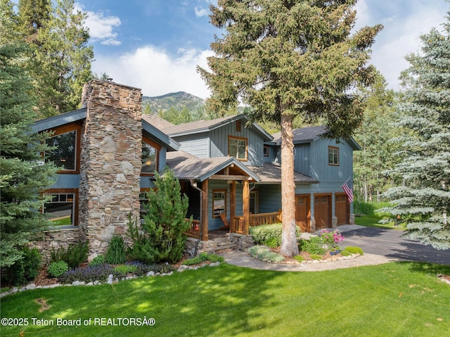 445 Aspen Ridge Trl, Alpine, WY 83128 - view of front of home featuring an attached garage, asphalt driveway, a chimney, a porch, and a front yard
