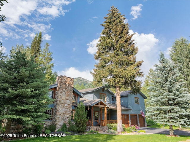 445 Aspen Ridge Trl, Alpine, WY 83128 - view of front of house featuring an attached garage, covered porch, driveway, a chimney, and a front lawn
