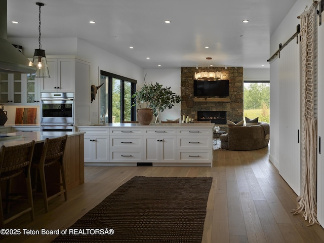 5060 W Eagle Rd, Wilson, WY 83014 - kitchen featuring stainless steel double oven, white cabinetry, light wood-type flooring, open floor plan, and a barn door