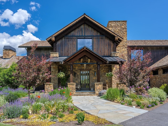 5060 W Eagle Rd, Wilson, WY 83014 - view of front facade with a chimney, stone siding, a standing seam roof, and a metal roof