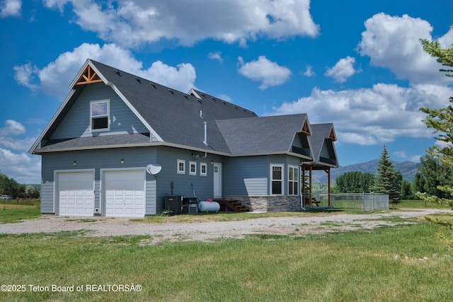 3139 Swan Valley Hwy, Swan Valley, ID 83449 - back of house featuring roof with shingles, stone siding, a garage, a mountain view, and a lawn