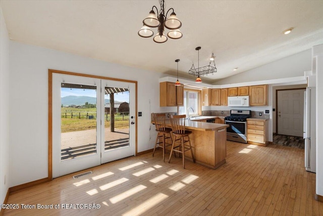 7302 Lakeside Rd, Victor, ID 83455 - kitchen with white appliances, a peninsula, vaulted ceiling, light wood-style floors, and hanging light fixtures